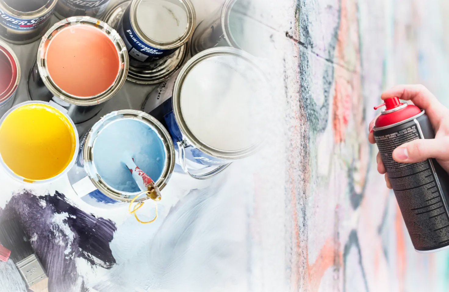 Gambar gabungan di mana tangan memegang kaleng cat semprot berwarna merah sedang menyemprotkan ke dinding bertekstur di sebelah kanan, dan kaleng cat kaleng yang terbuka dengan berbagai warna (biru muda, kuning, oranye, putih) di sebelah kiri. Ini melambangkan sumber-sumber senyawa organik volatil (VOC).
